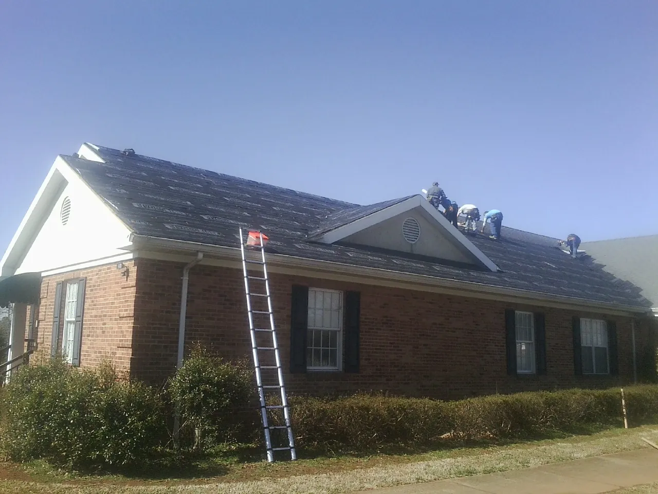 Crew tearing shingles off a brick ranch roof with a ladder set — Emergency Roof Repair work by our crew in Sebeka