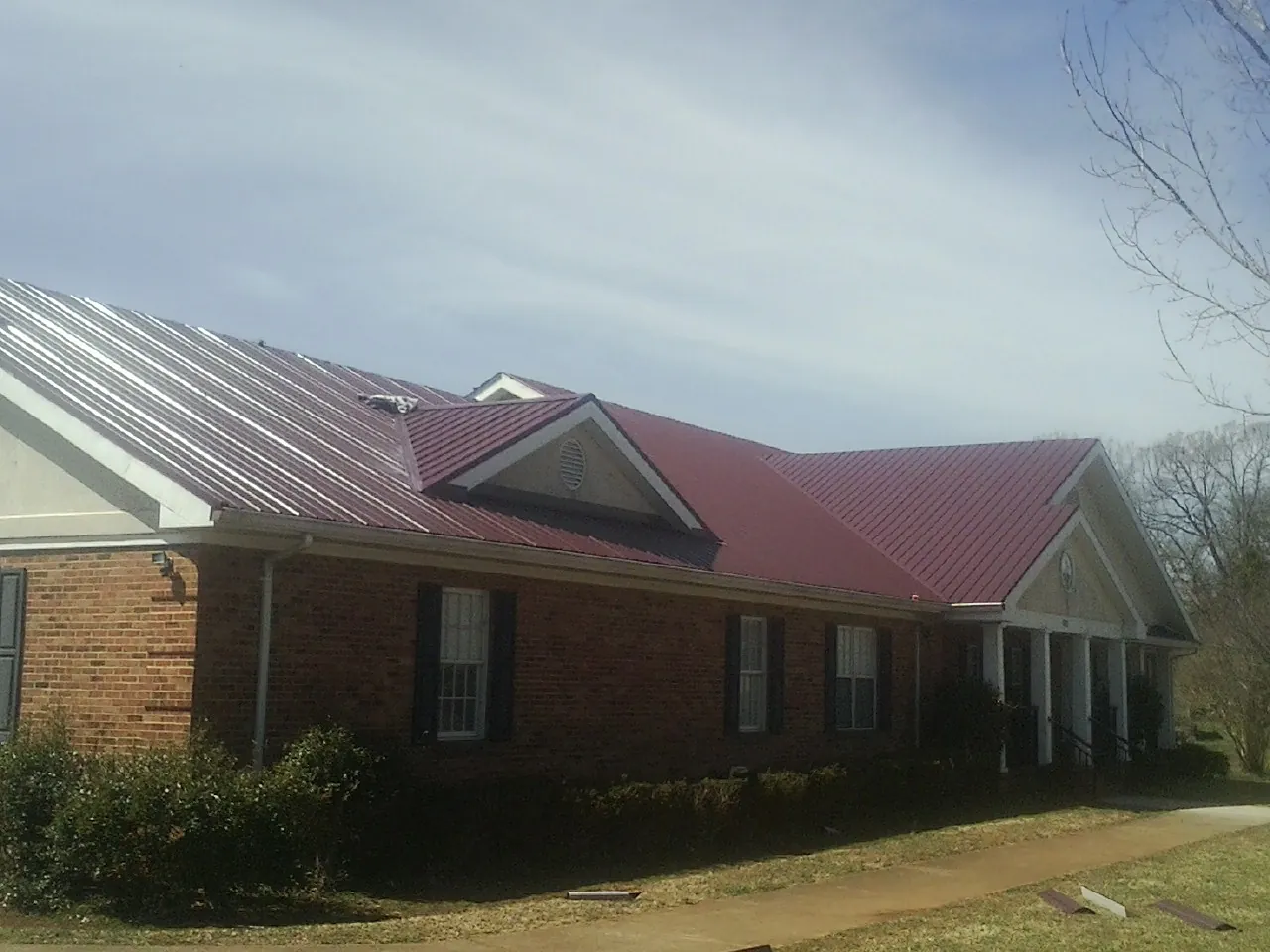 Red metal roof with gabled entries on a long brick building, from a Hail Damage Roof Repair job in Sebeka