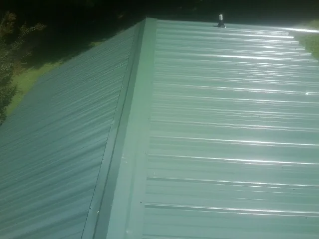 New green metal panels meeting at the ridge of a roof — Flat Roof Repair work by our crew in Sebeka