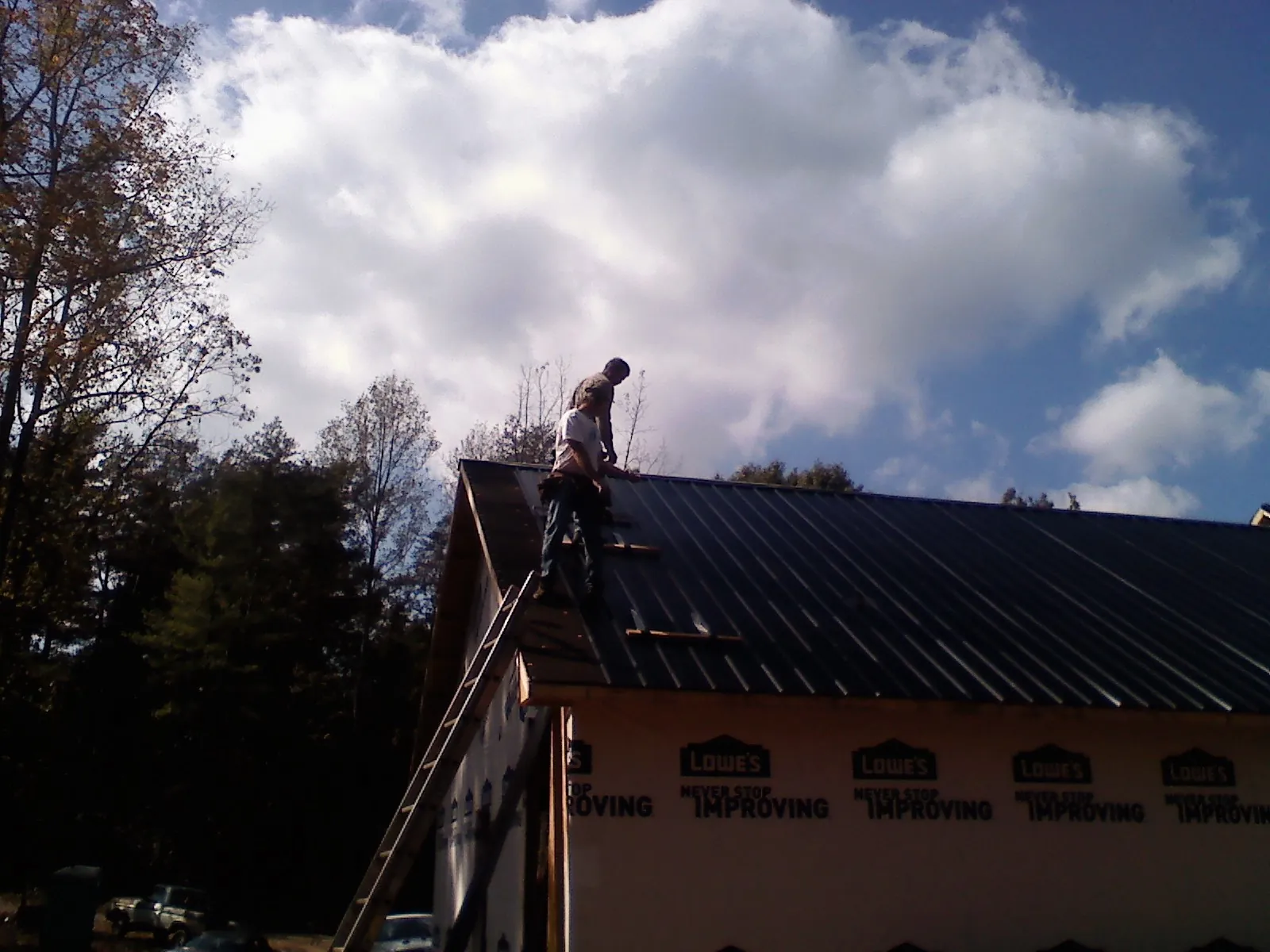 Roofer fastening dark metal panels high against a cloudy sky, from a Roof Inspection job in Sebeka