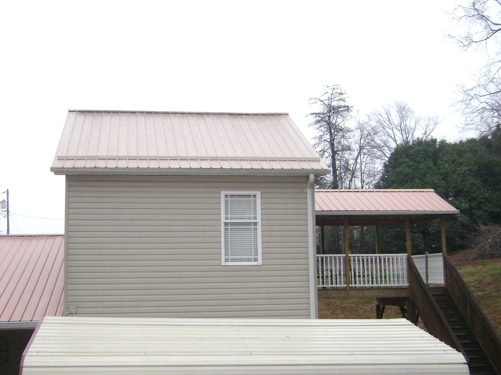 Tan metal roofs on a two story addition and attached porch, from a Roof Replacement job in Sebeka